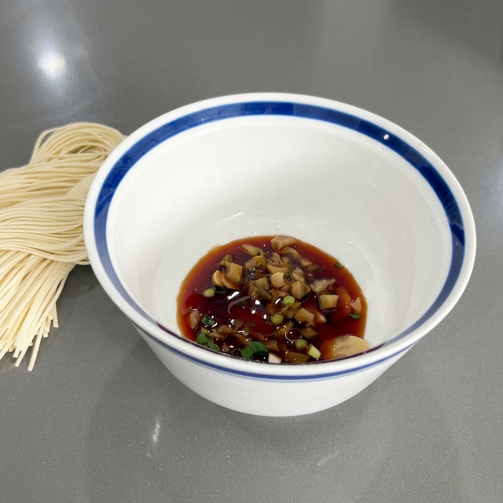 La ciotola con salsa di soia, cipollotti e aromatici, che mostra una leggera lucentezza dovuta allolio di sesamo aggiunto.