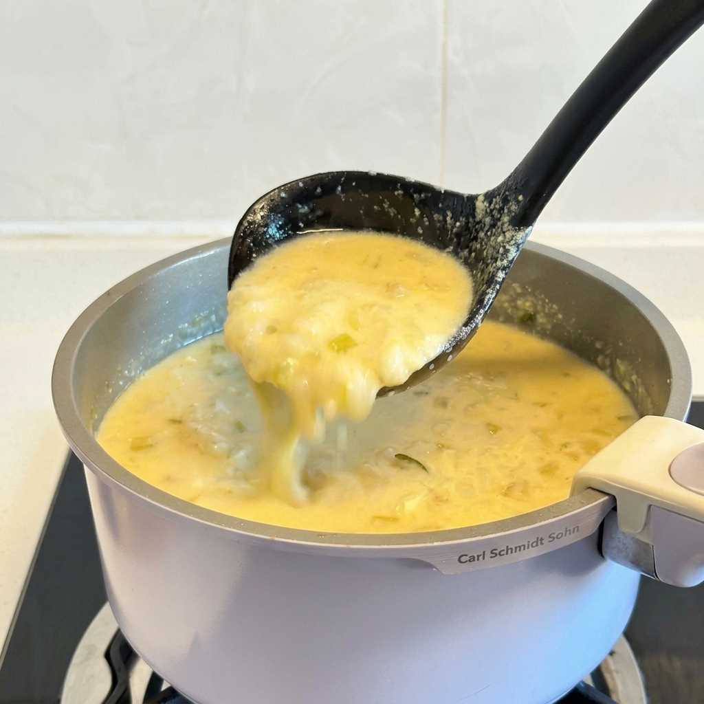 Un mestolo nero che solleva una porzione di densa e cremosa zuppa di pollo al limone greca da una pentola.