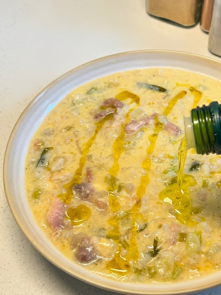 Olio doliva dorato versato da una bottiglia verde su un piatto di cremosa zuppa di pollo al limone.