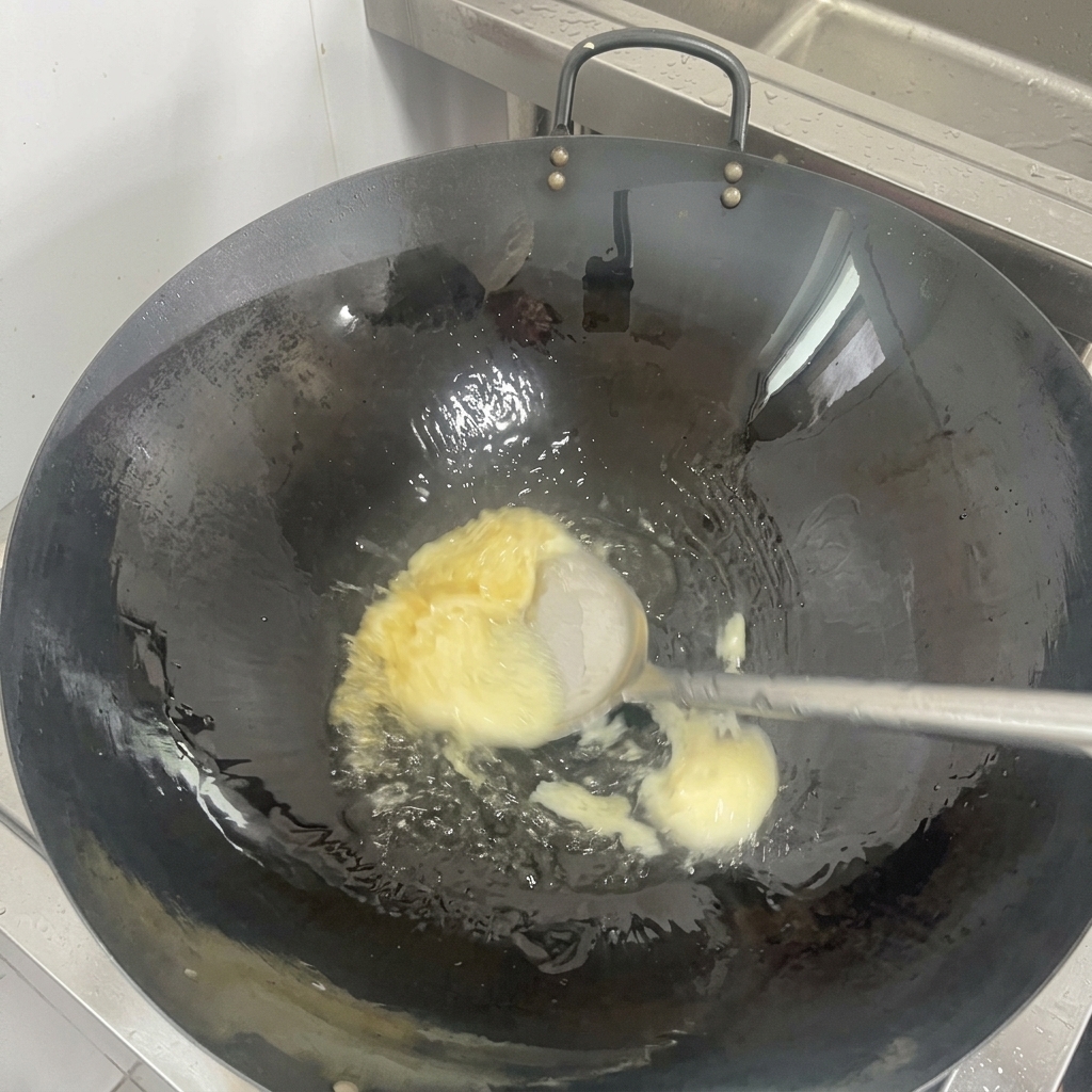 Un pezzo solido di strutto bianco che si scioglie diventando olio trasparente sul fondo di un wok nero ben oliato.