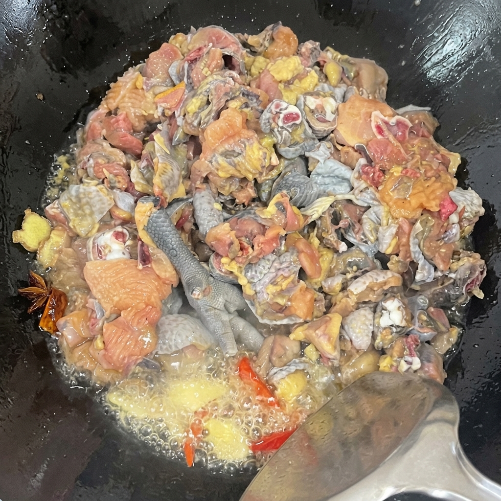 Un primo piano dei pezzi di pollo moroseta saltati in un wok con spezie, che mostra lolio che sfrigola durante la cottura.