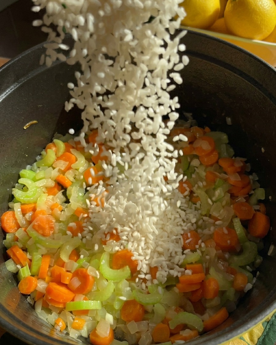 Una pioggia di chicchi di riso jasmine bianco che viene versata nella pentola con il mix di carote, sedano e cipolle soffritte.
