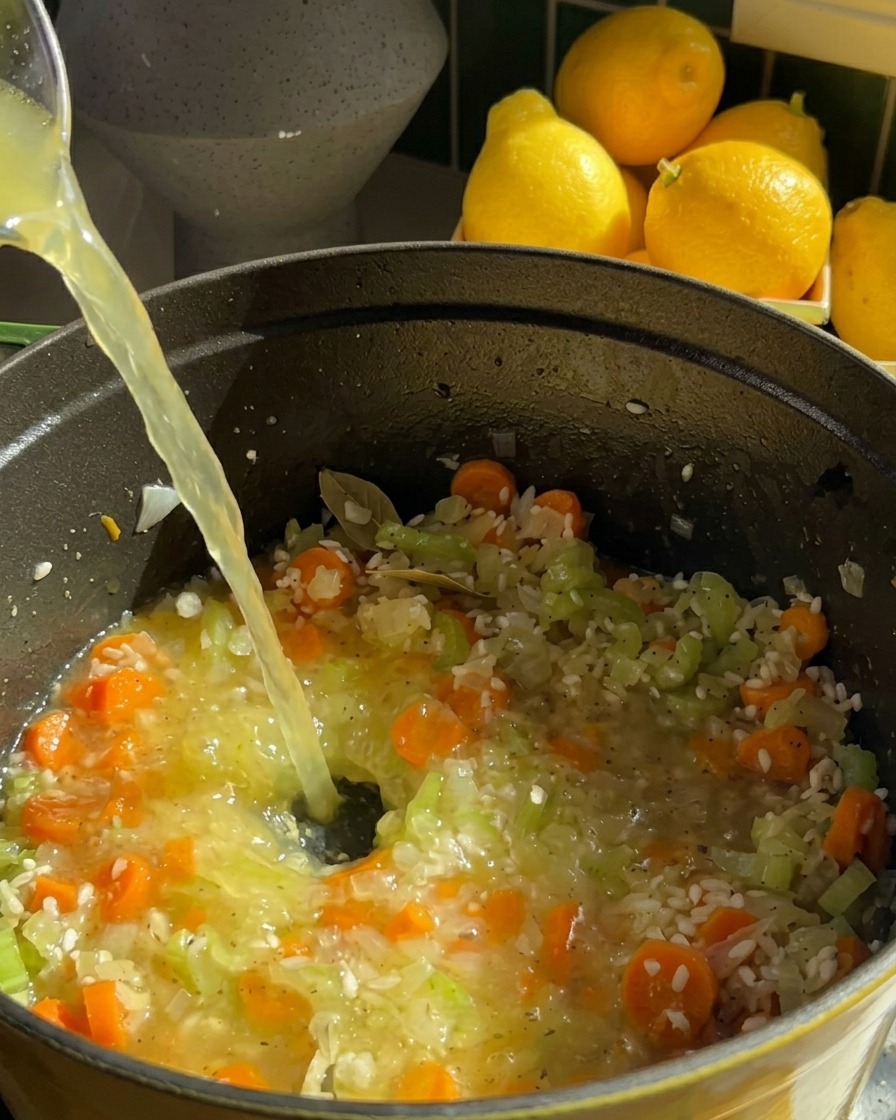 Un flusso di brodo di pollo limpido versato direttamente nella pentola per coprire riso, carote e sedano.