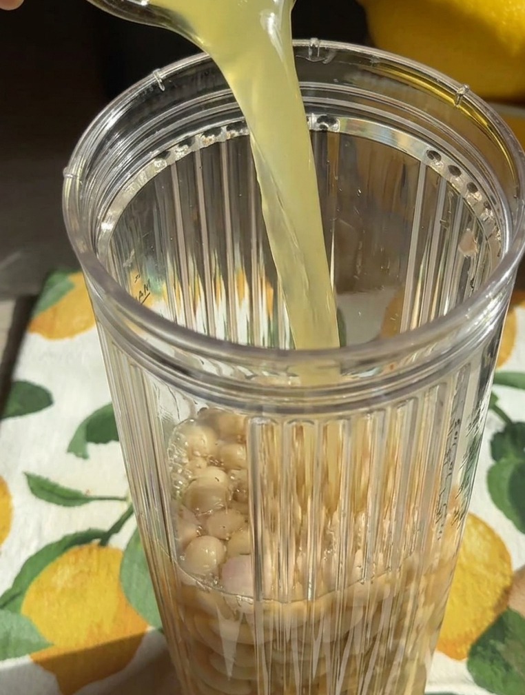 Un liquido dorato versato da un bicchiere nel frullatore insieme ai fagioli bianchi interi.