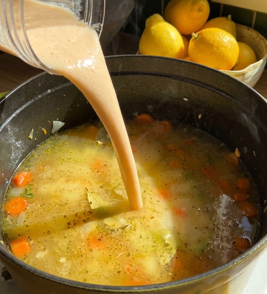 Un flusso di crema di fagioli densa e beige versata dal frullatore nella pentola dove sobbolle la zuppa con le carote.