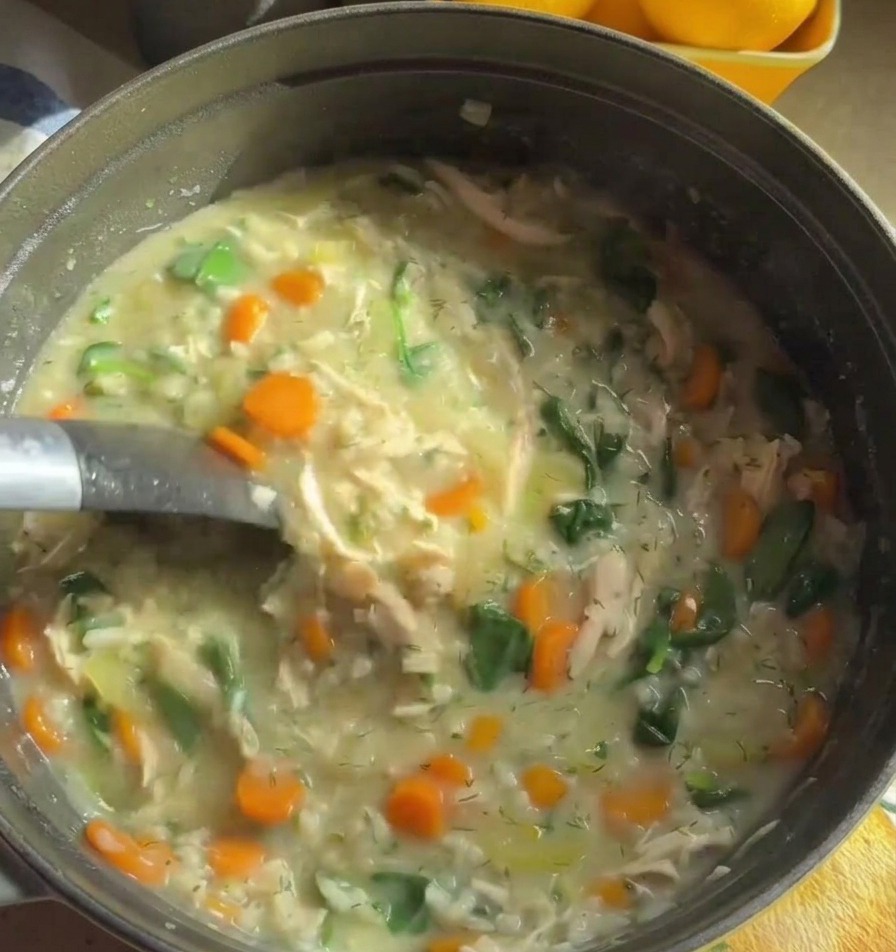 Un mestolo di metallo che solleva la densa zuppa di pollo cremosa con carote arancioni e spinaci verdi.