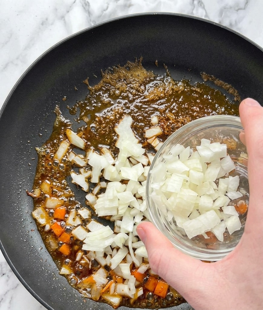 Cipolla bianca a cubetti versata da una ciotola di vetro in una padella con olio e fondo di cottura del salmone.