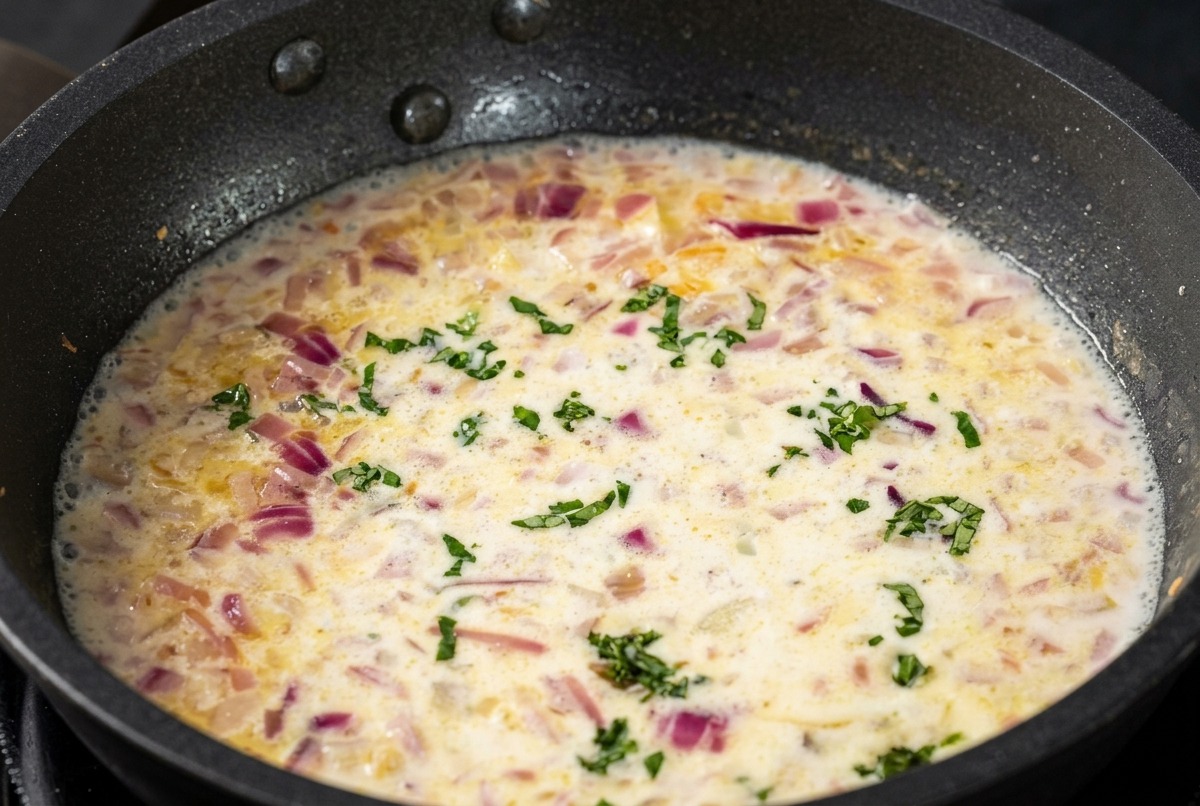 Una salsa bianca e cremosa in padella con pezzetti di basilico verde tritato sparsi uniformemente.