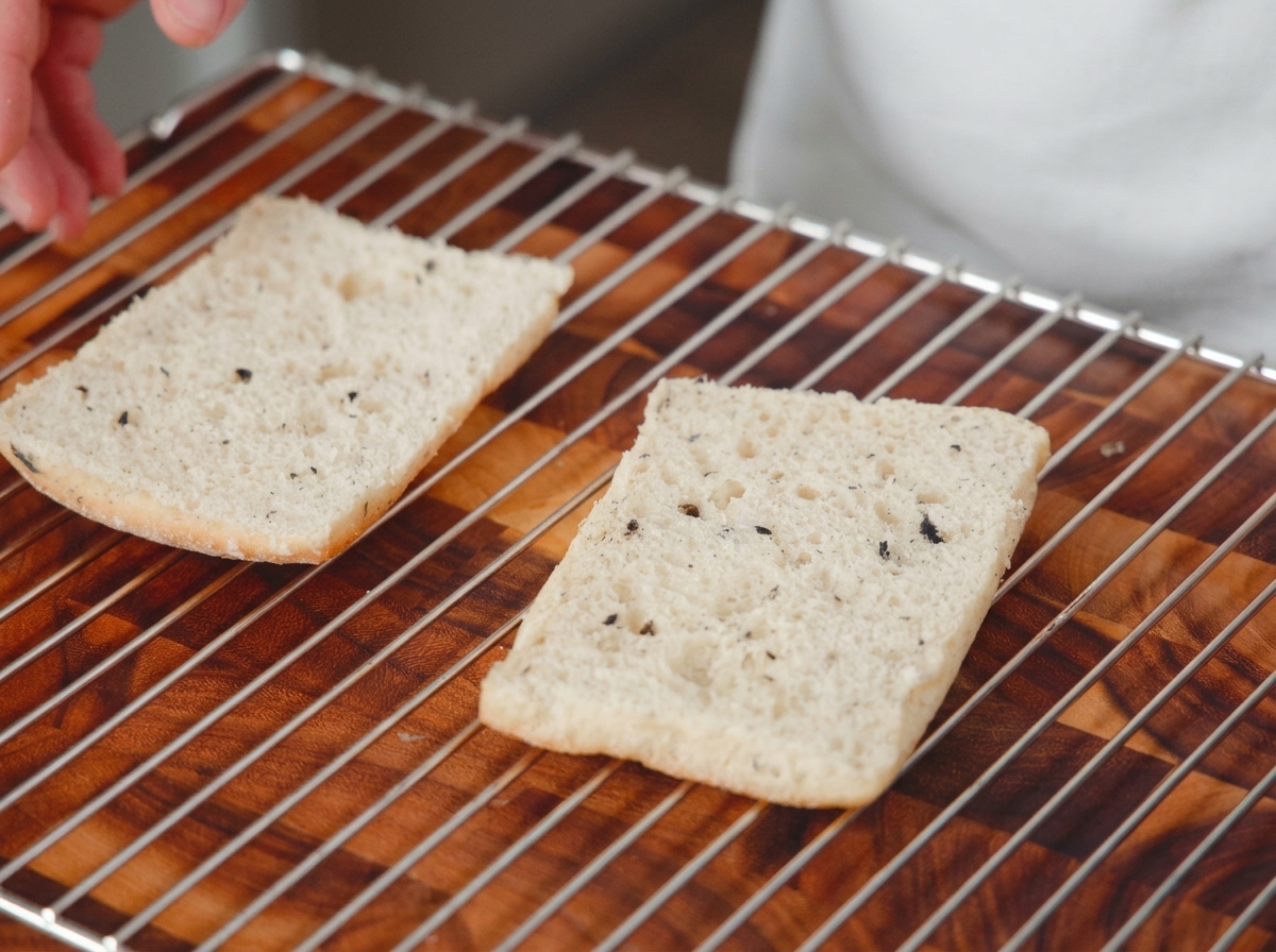 Due metà di pane affettato disposte sulla griglia del forno sopra una superficie di legno, pronte per essere tostate.