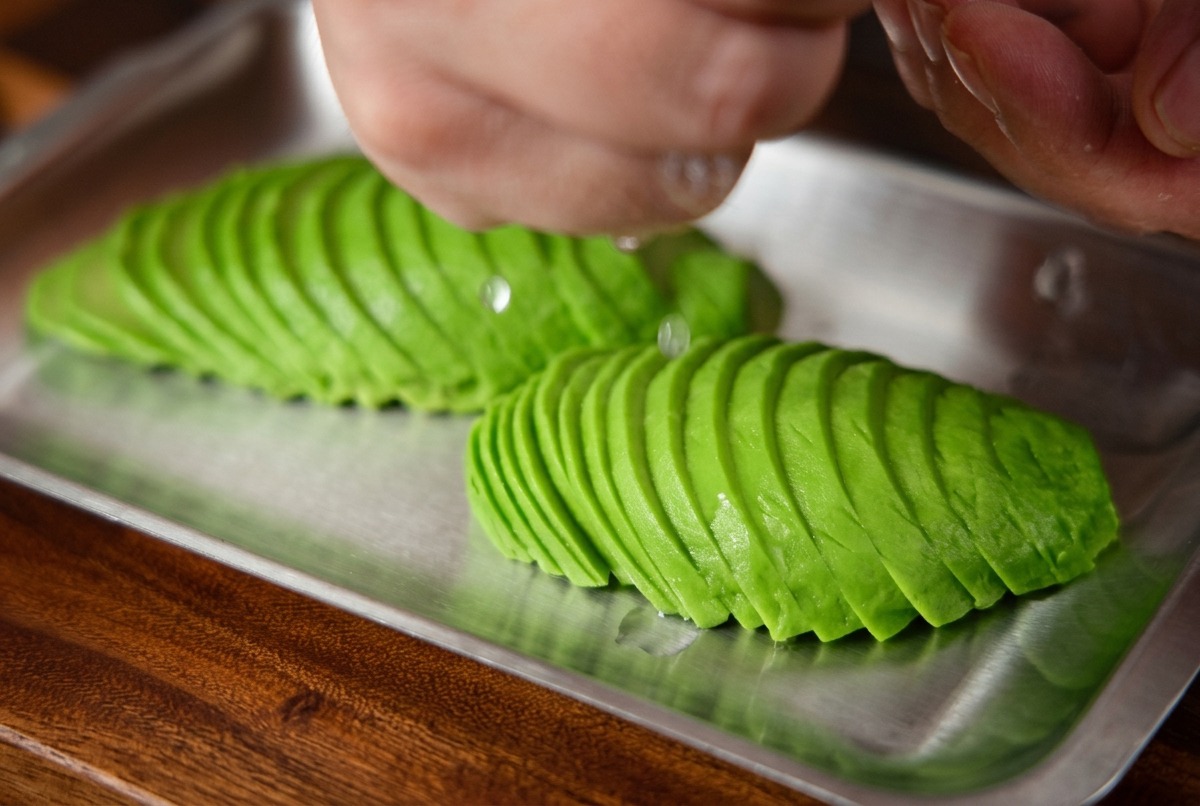 Succo di limone fresco spremuto a mano su un vassoio di fette di avocado disposte ordinatamente.