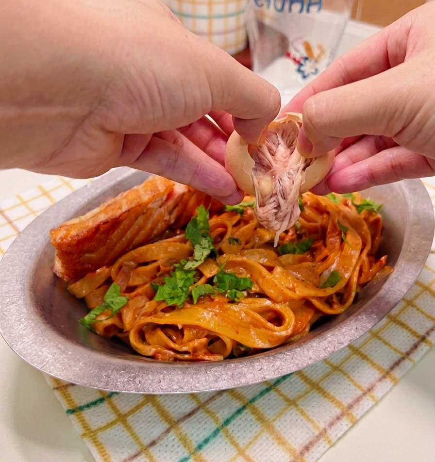 Mani che sgusciano con cura e adagiano un uovo bazzotto su un piatto di pasta alla crema piccante con salmone scottato.