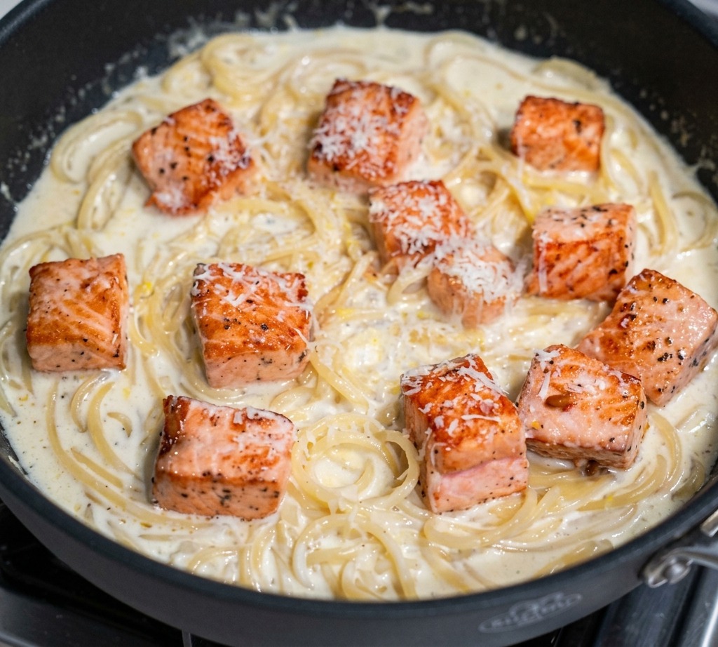 Parmigiano Reggiano grattugiato finemente sopra cubetti di salmone e pasta cremosa in padella.
