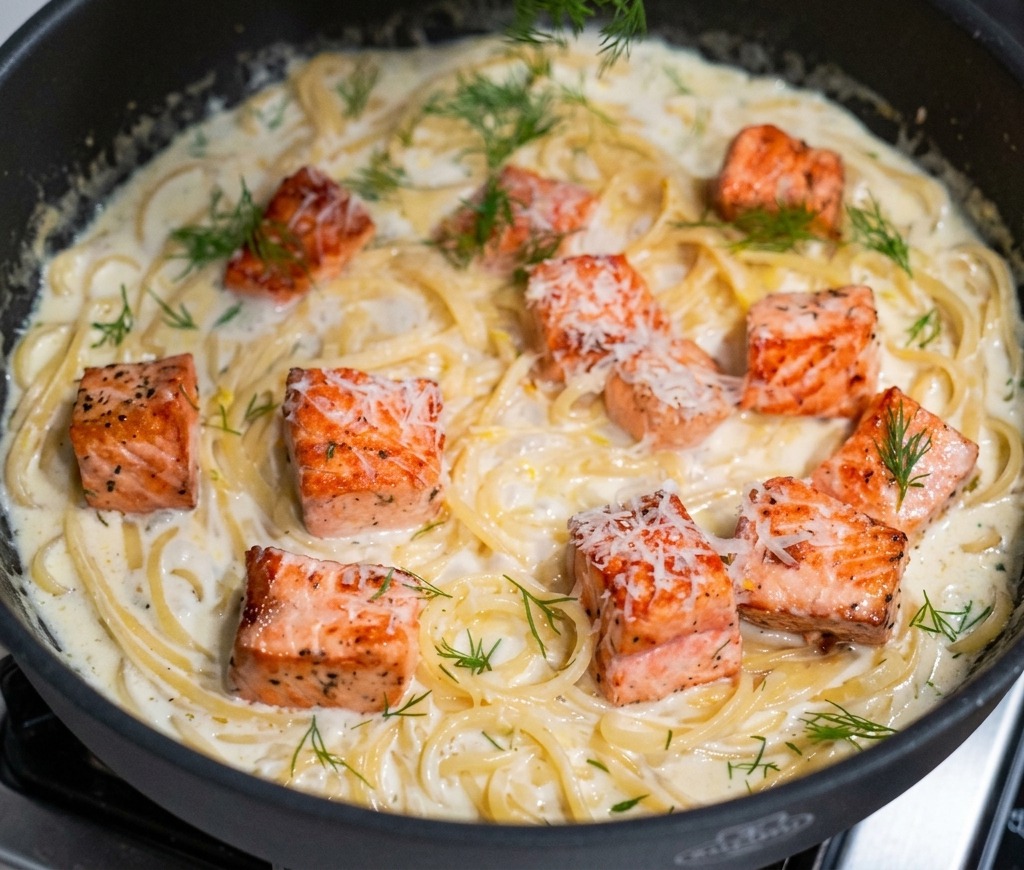Una mano che sparge aneto verde tritato su una padella di pasta cremosa al salmone appena finita.