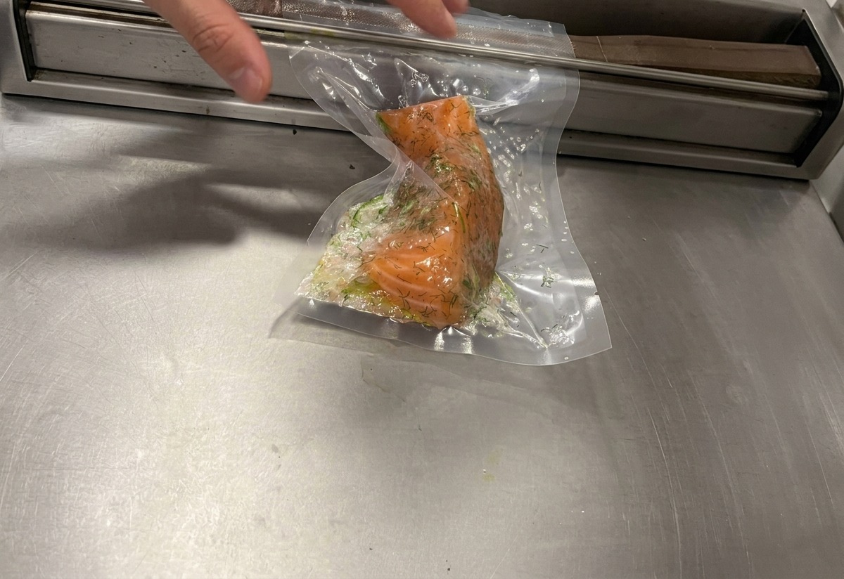 Una macchina per il sottovuoto che rimuove laria da un sacchetto di plastica contenente un filetto di salmone in crosta di erbe.