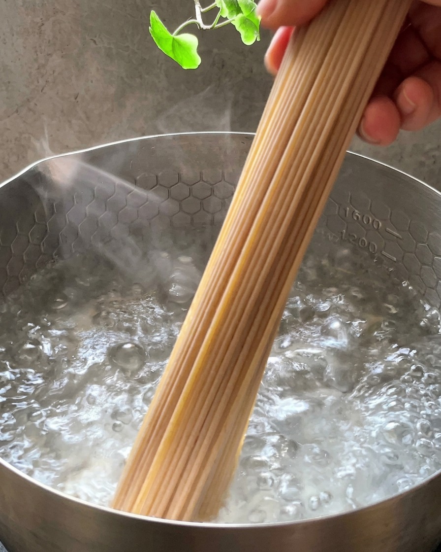 Un mazzo di spaghetti integrali crudi che viene immerso in una pentola dacciaio con acqua bollente.
