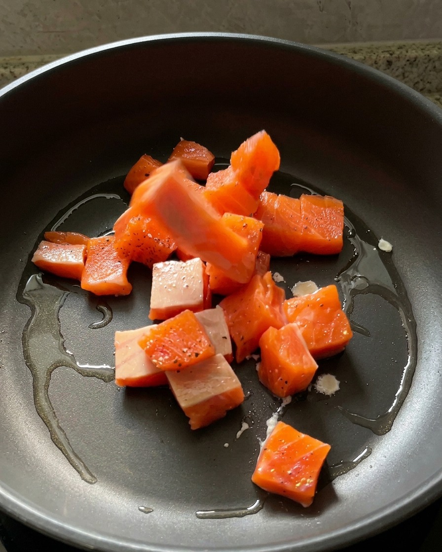 Cubetti di salmone crudo marinato che vengono adagiati in una padella calda con olio lucido.