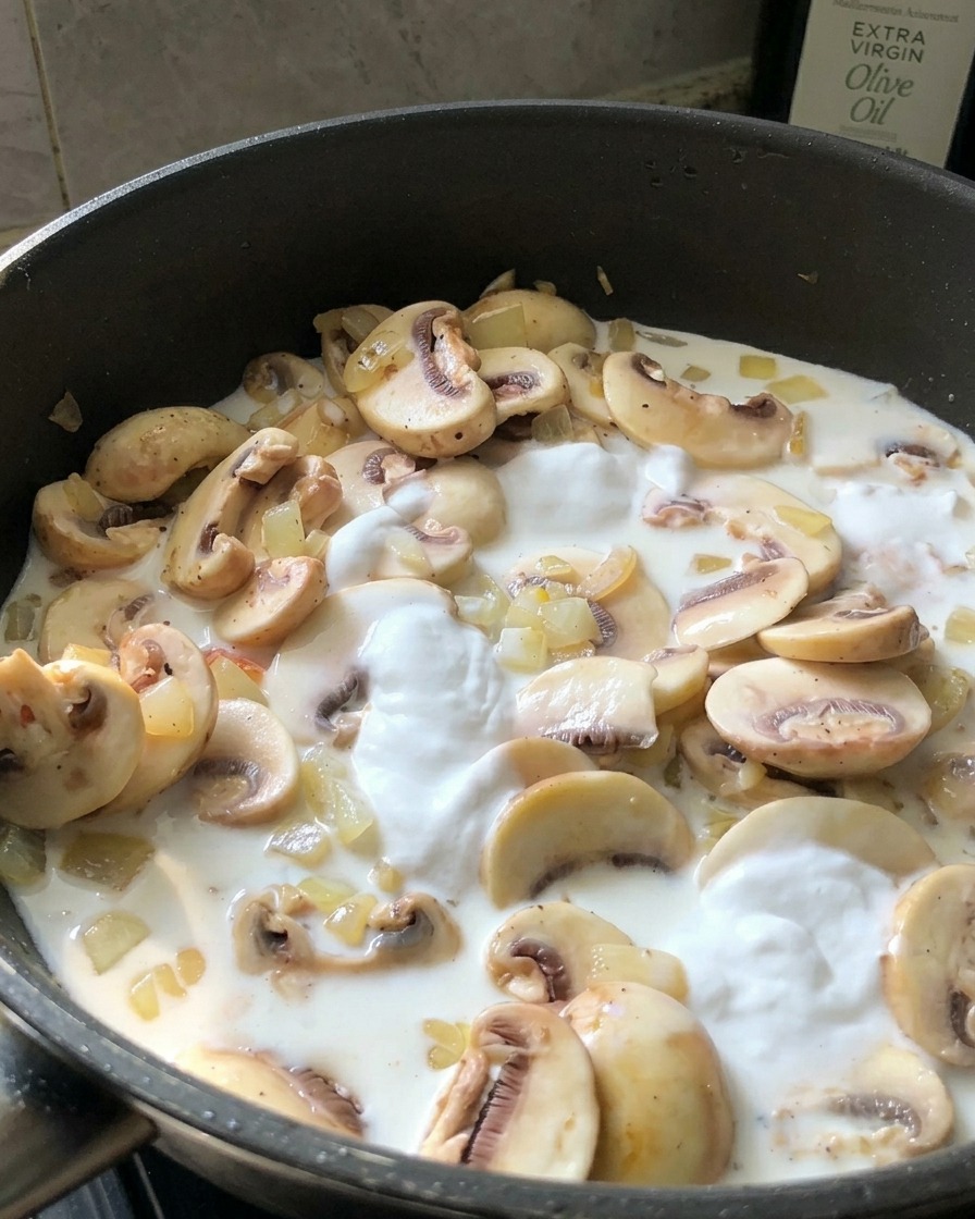 Una persona che assaggia una salsa alla panna bianca con un cucchiaino da una padella nera contenente funghi.