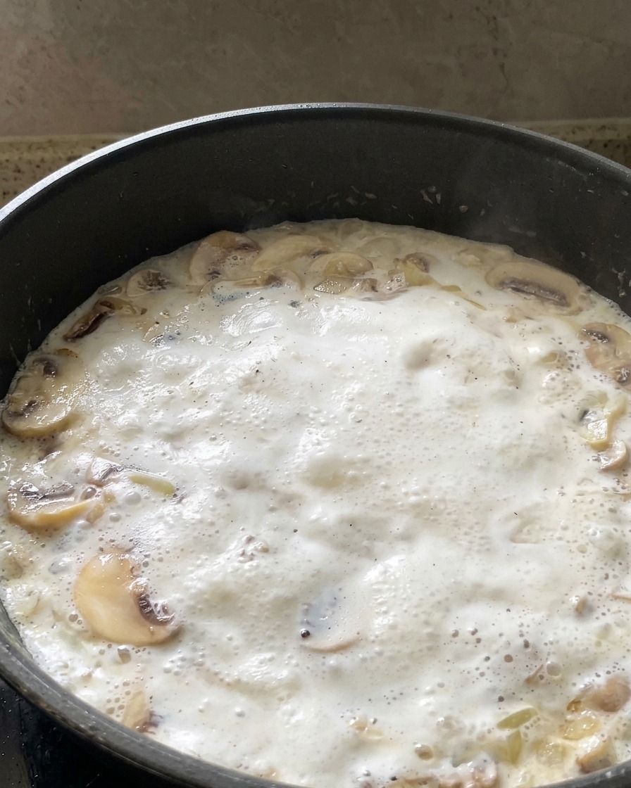 Foglie di spinaci verdi freschi aggiunte a una salsa di funghi alla panna che sobbolle in padella.