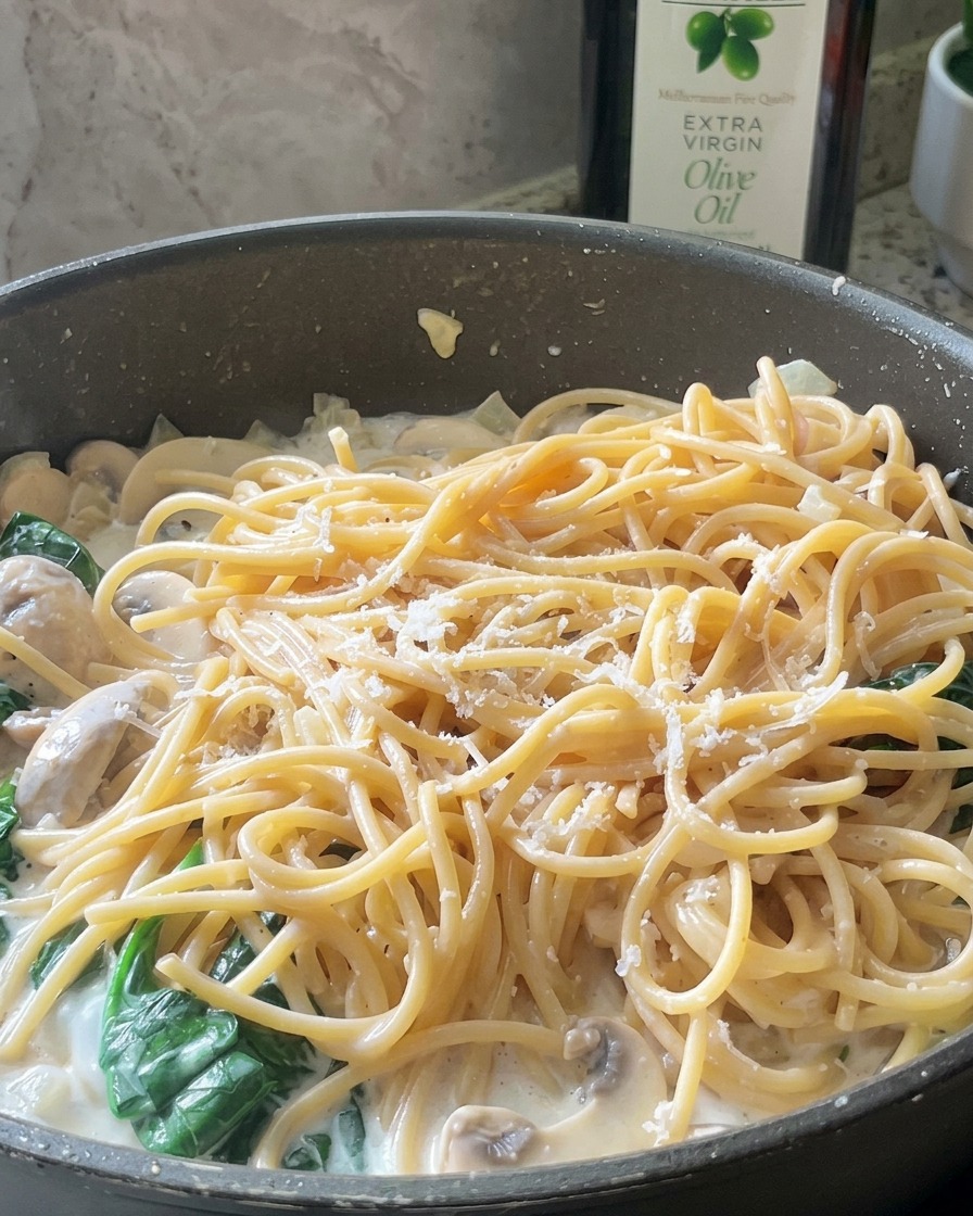 Scaglie sottili di parmigiano grattugiato sparse su una padella di spaghetti cremosi con funghi e spinaci.