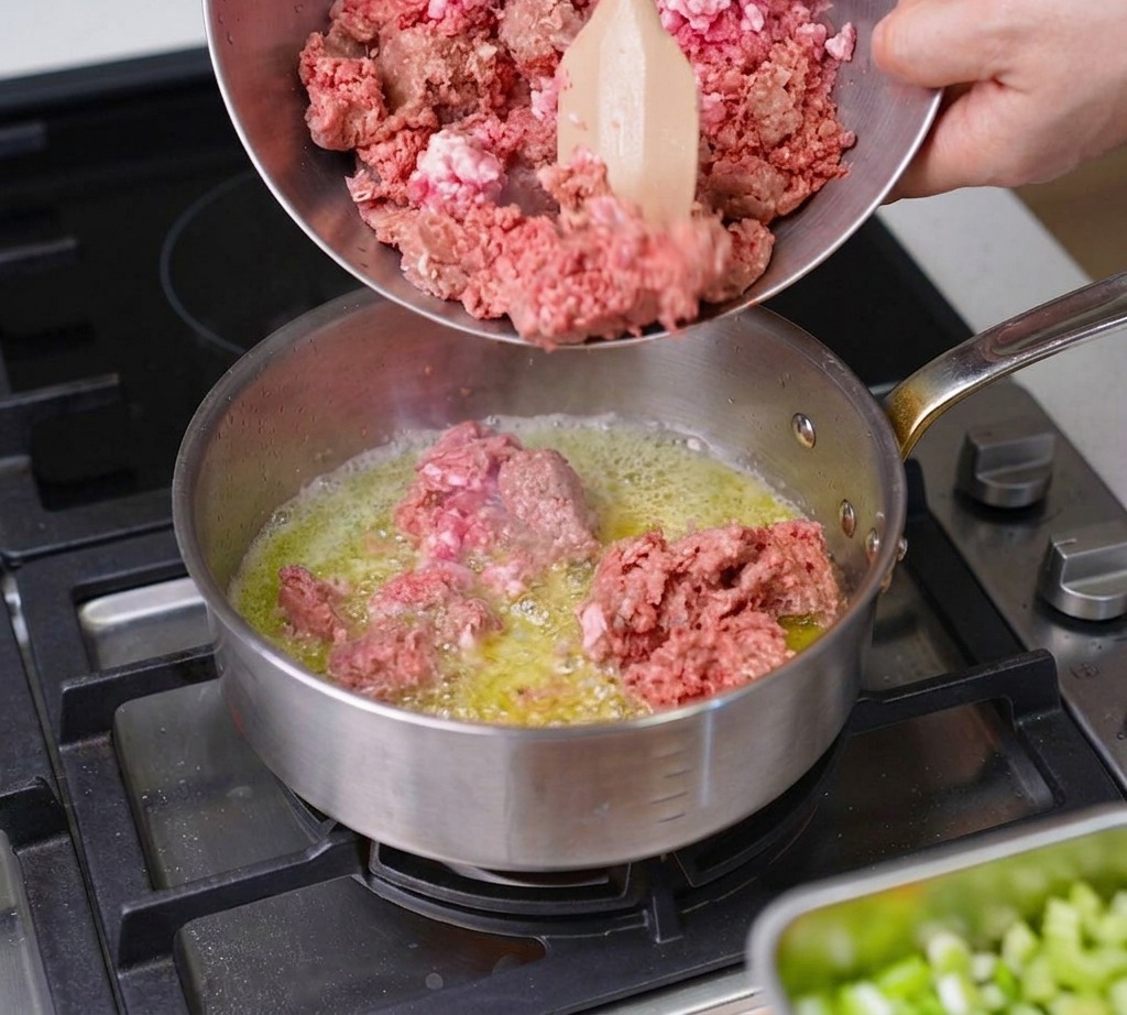 Carne macinata di manzo e maiale versata da una ciotola di metallo in una casseruola sfrigolante con burro fuso.