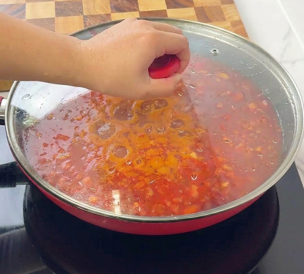 Una persona che posiziona un coperchio di vetro trasparente su una padella rossa colma di ragù bolognese.