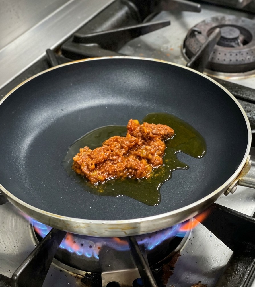 Una generosa porzione di ragù di carne adagiata sullolio doliva al centro di una padella sul fuoco.