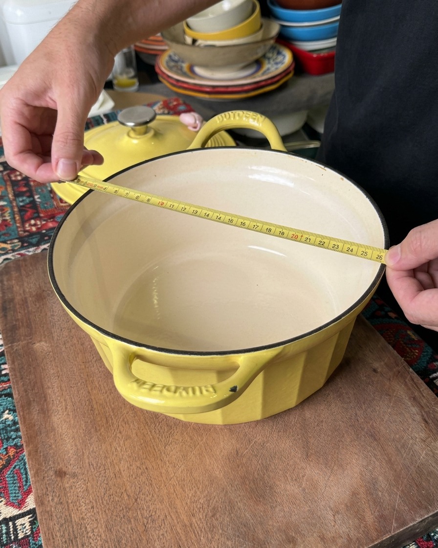 Una persona misura il diametro superiore di una casseruola gialla con un metro da sarto giallo per confermare che sia larga circa 26 centimetri.