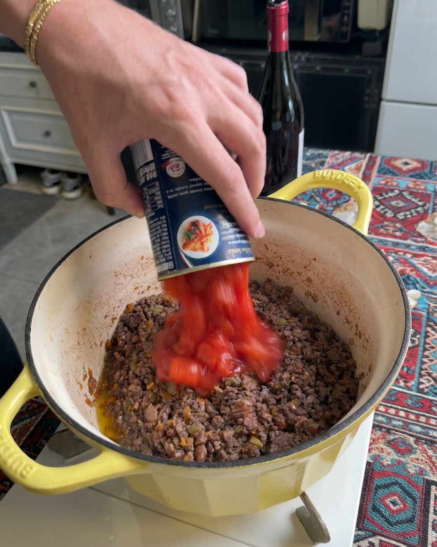 Passata di pomodoro che viene versata nella pentola con la carne rosolata.