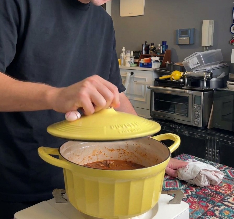 Una persona posiziona il coperchio di ghisa giallo sopra la pentola del ragù per iniziare la cottura lenta.