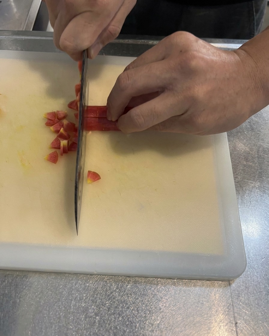 Mani che tagliano una carota arancione brillante a piccoli cubetti regolari su un tagliere bianco usando un coltello da cucina.