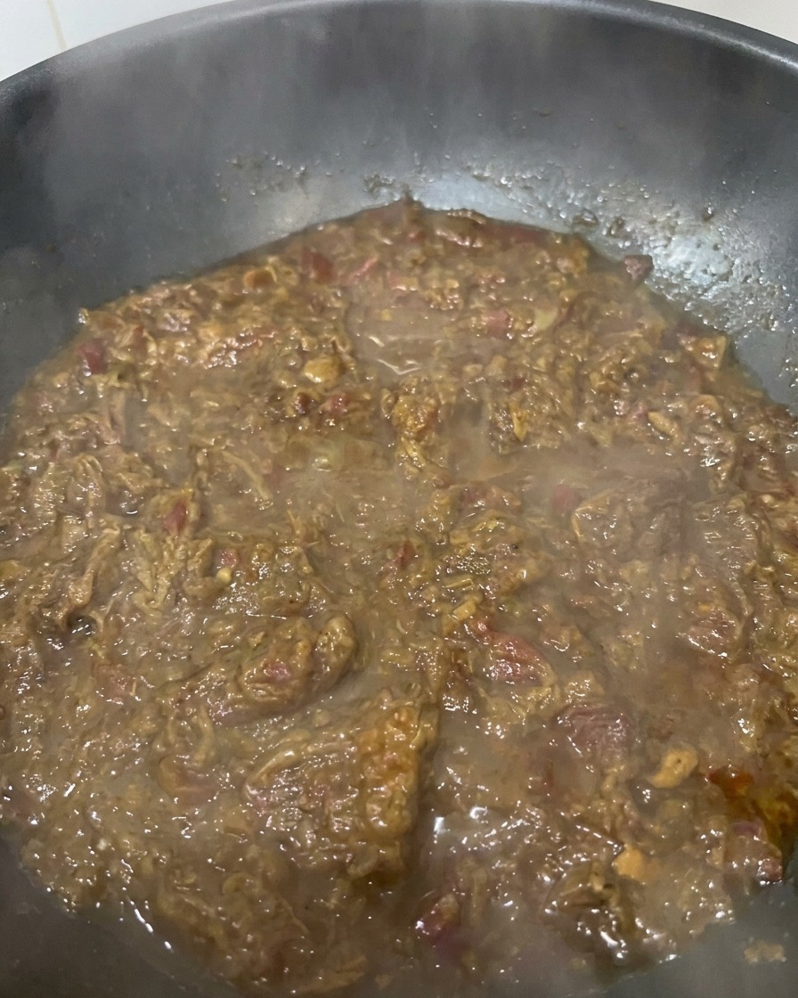 Un primo piano di un sugo denso color marrone scuro a base di cipolle e carne che sobbolle in pentola, mostrando una consistenza ricca e vellutata.