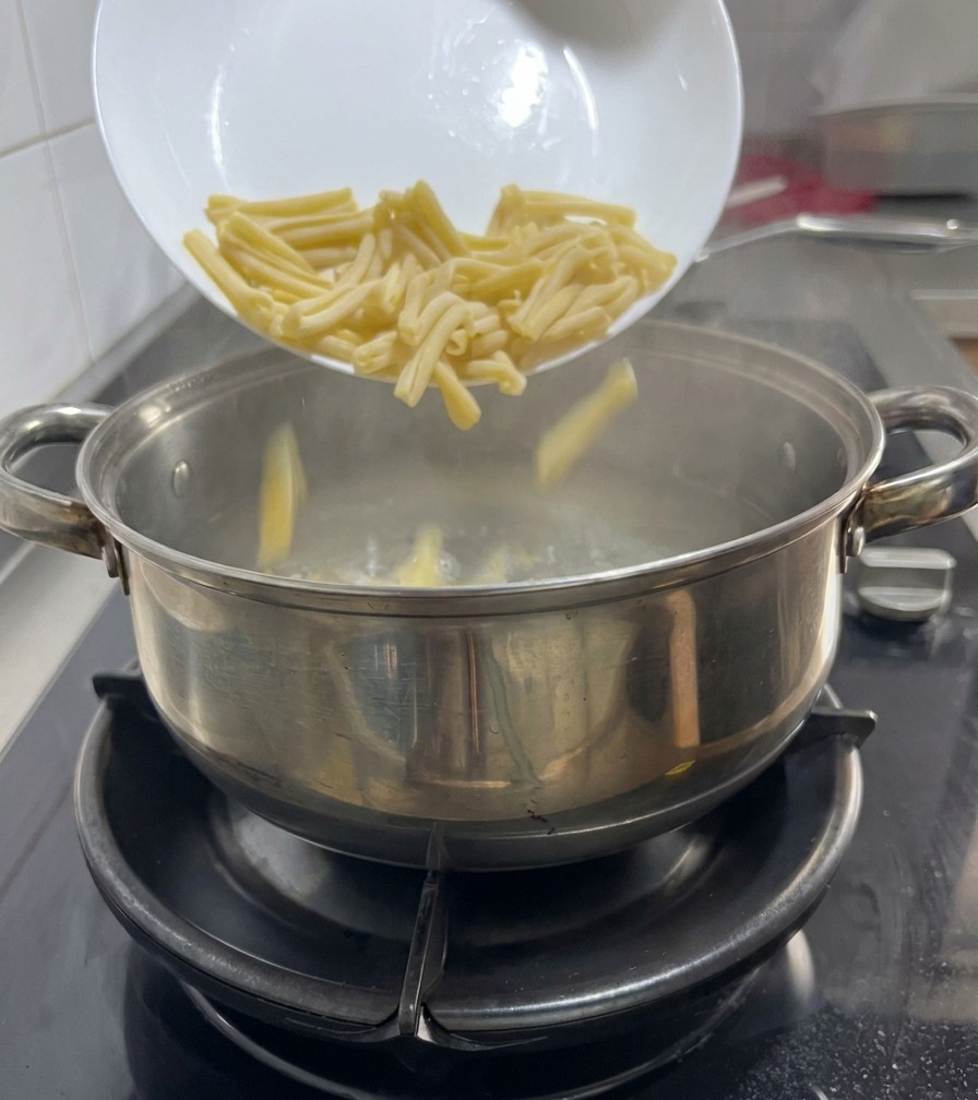 Pasta formato casarecce che viene versata da un piatto bianco in una pentola di acqua bollente su un fornello a gas.