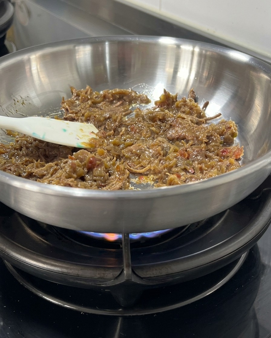 Un denso sugo di carne e filamenti di manzo saltati con una spatola in una padella dacciaio inossidabile sulla fiamma.