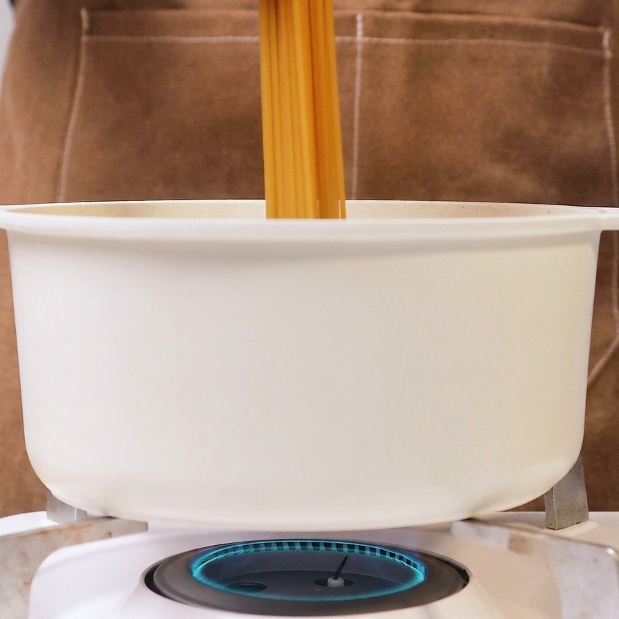 Una persona inserisce gli spaghetti interi in una pentola bianca di acqua bollente su un fornello a gas.