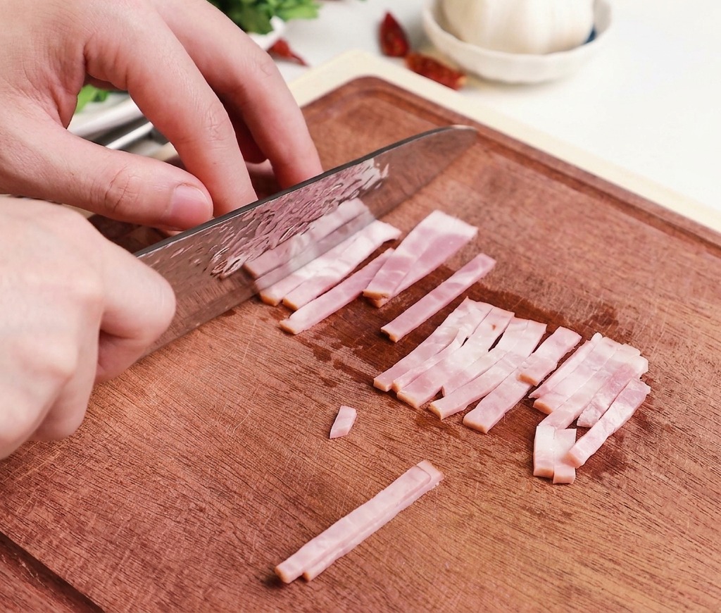 Mani che usano un coltello da chef professionale per tagliare strisce di bacon crudo in piccoli pezzi uniformi su un tagliere di legno.