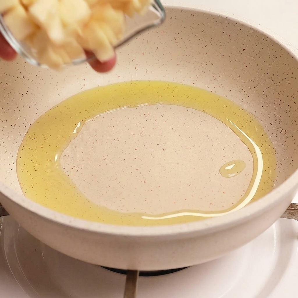 Una ciotolina di vetro versa lamelle di aglio fresco in una padella contenente olio doliva caldo e sfrigolante.