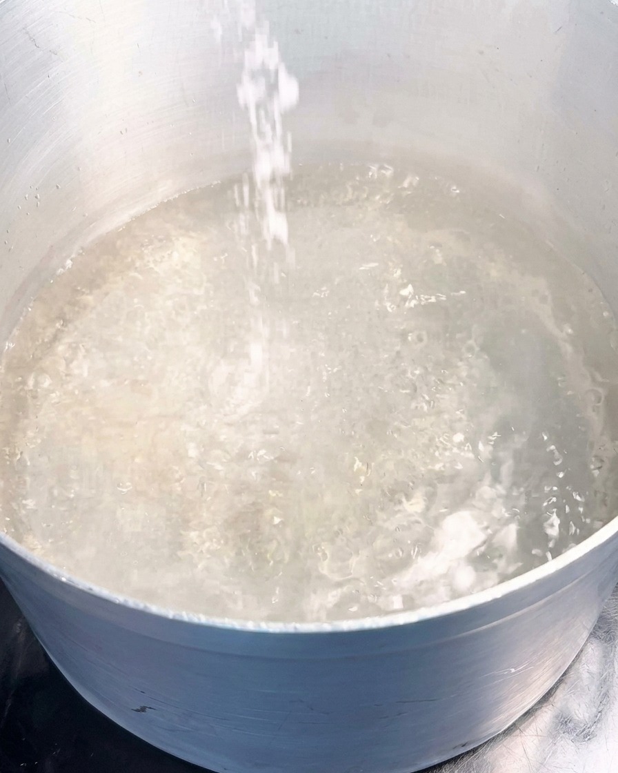Un flusso di sale marino bianco viene versato in una pentola dacqua che bolle vigorosamente.