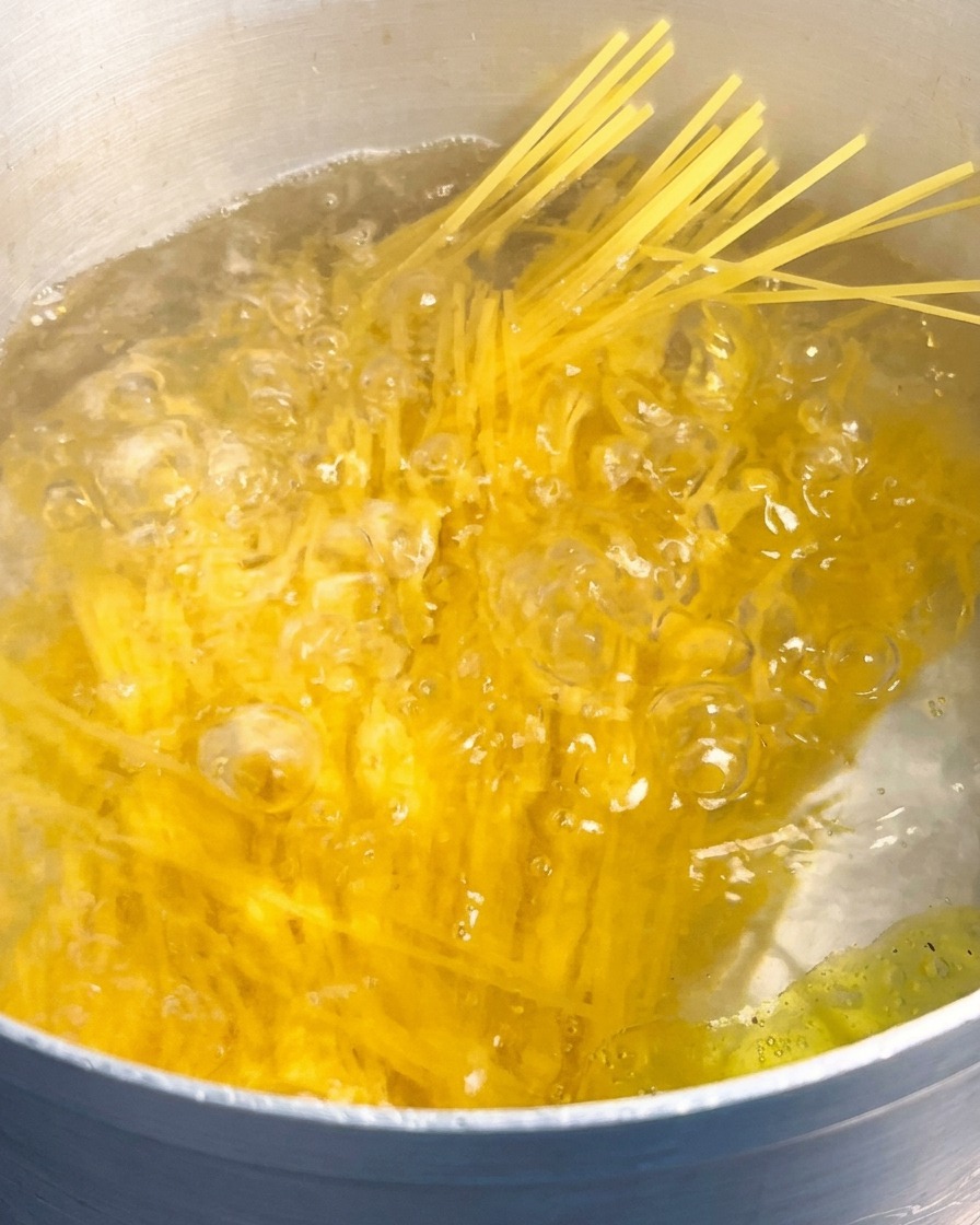 Un mazzo di spaghetti gialli secchi viene immerso in una grande pentola dacqua in piena ebollizione.