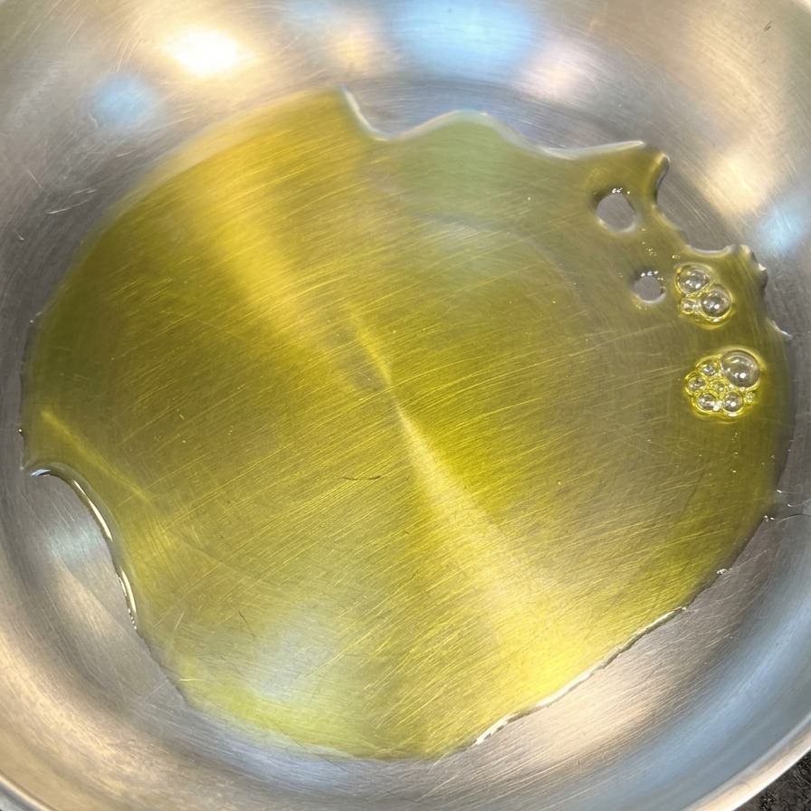 Un velo di olio doliva giallo e brillante riveste il fondo di una padella pulita in acciaio inossidabile.