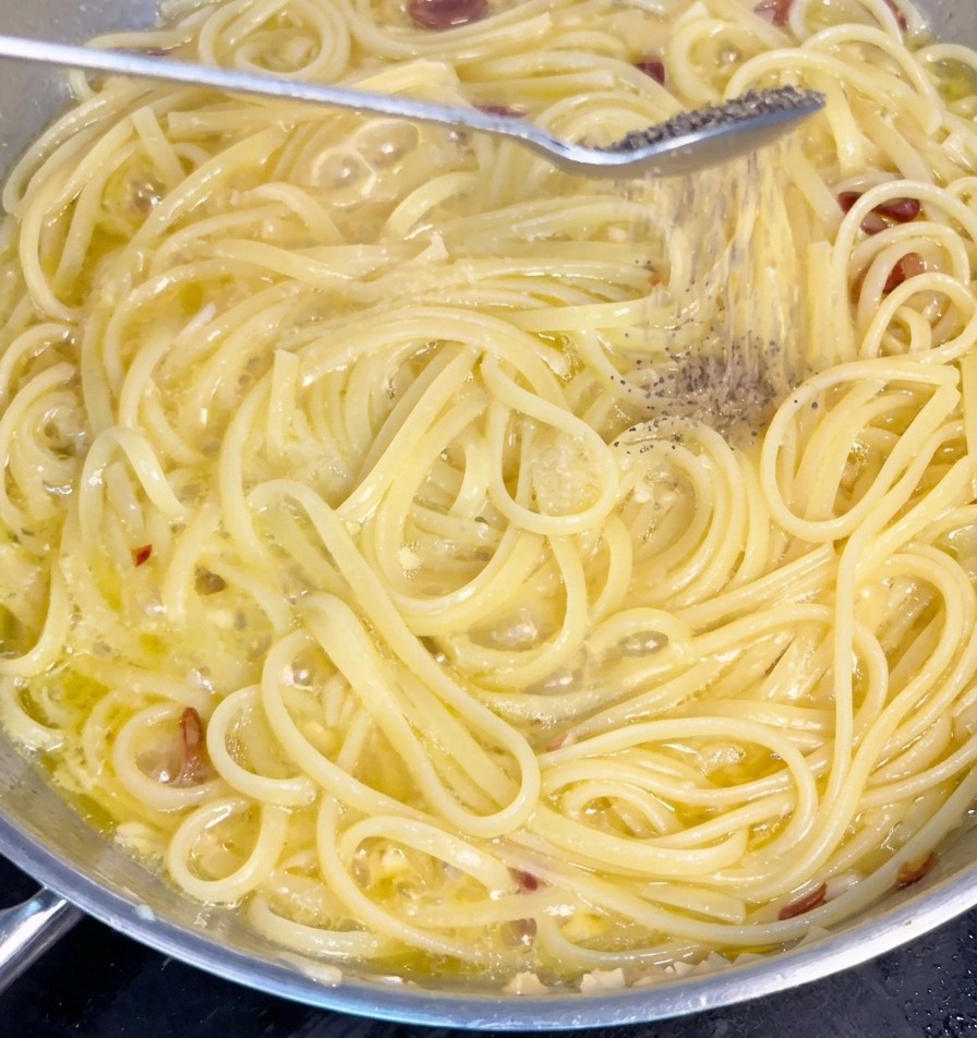 Pepe nero macinato fresco cade da un cucchiaio sugli spaghetti che sobbollono nel sugo di aglio e olio.