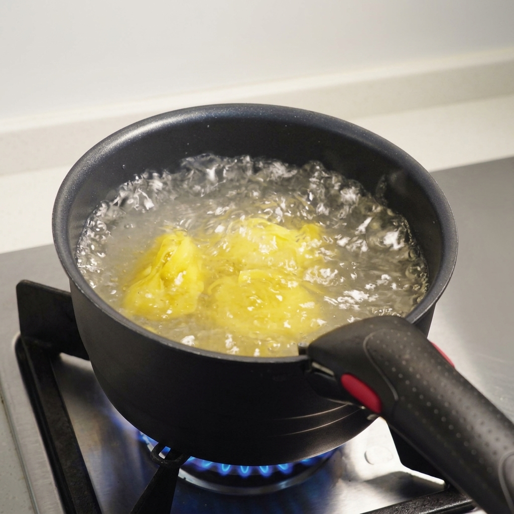 Fettuccine immerse in acqua bollente e salata allinterno di una pentola scura su un fornello a gas.