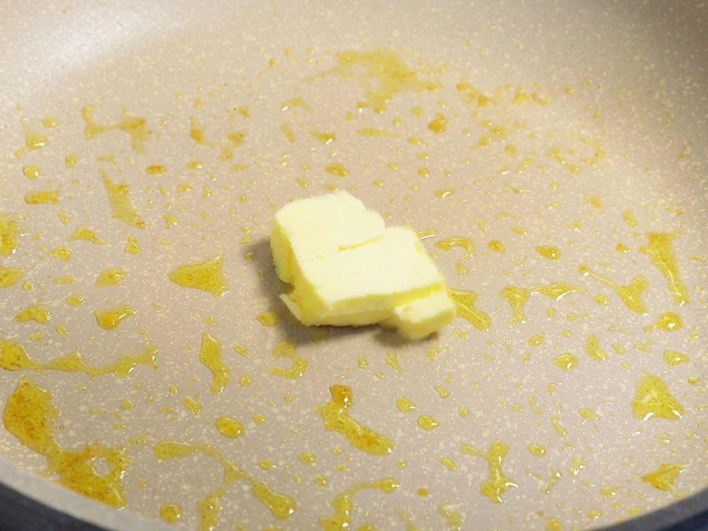Un piccolo pezzetto di burro giallo che si scioglie in una padella con i residui dellolio di cottura.