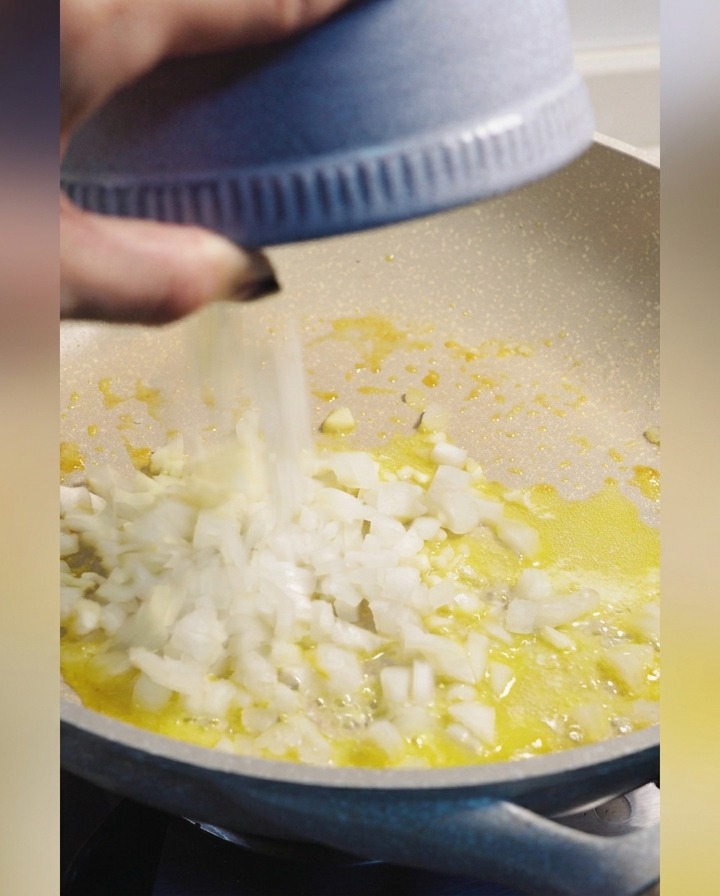 Cipolla bianca tritata aggiunta da una ciotola blu in una padella con burro fuso.
