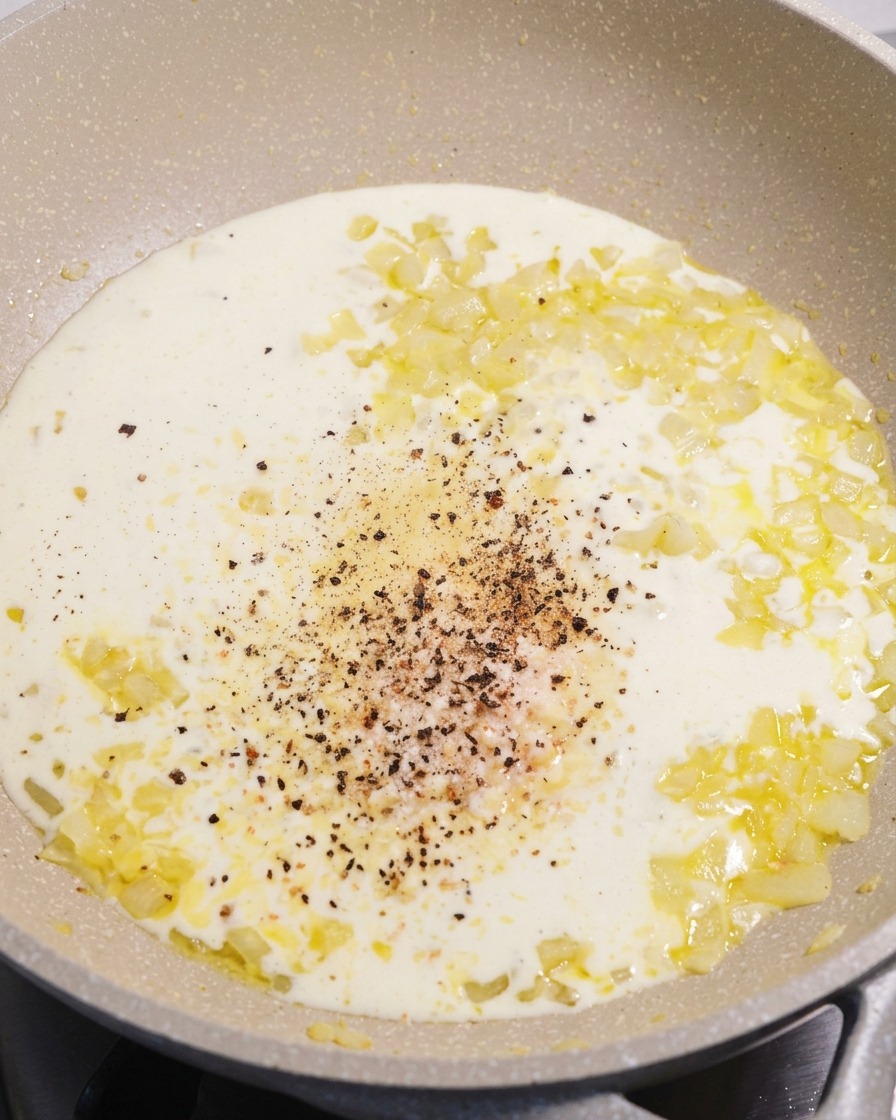 Una padella con una salsa alla panna bianca e vellutata, con al centro pepe nero macinato fresco e parmigiano.