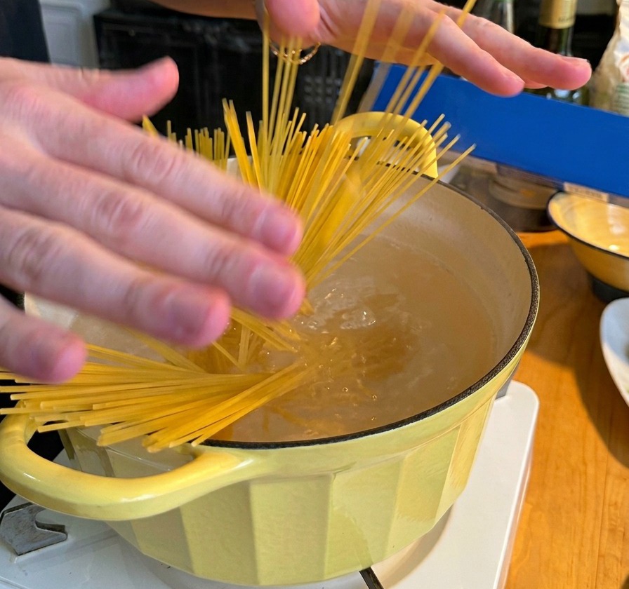 Una persona che tuffa un nido di spaghetti secchi in una pentola gialla colma di acqua in ebollizione.