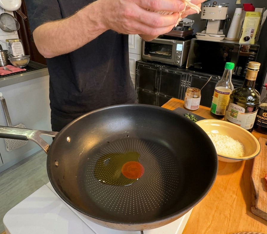 Una persona che versa una manciata di cipolla bianca affettata in una padella con olio doliva caldo.