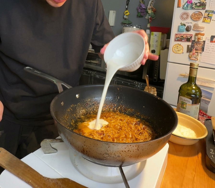 Panna liquida versata in una padella contenente una salsa densa e rossastra a base di olio piccante e cipolle.