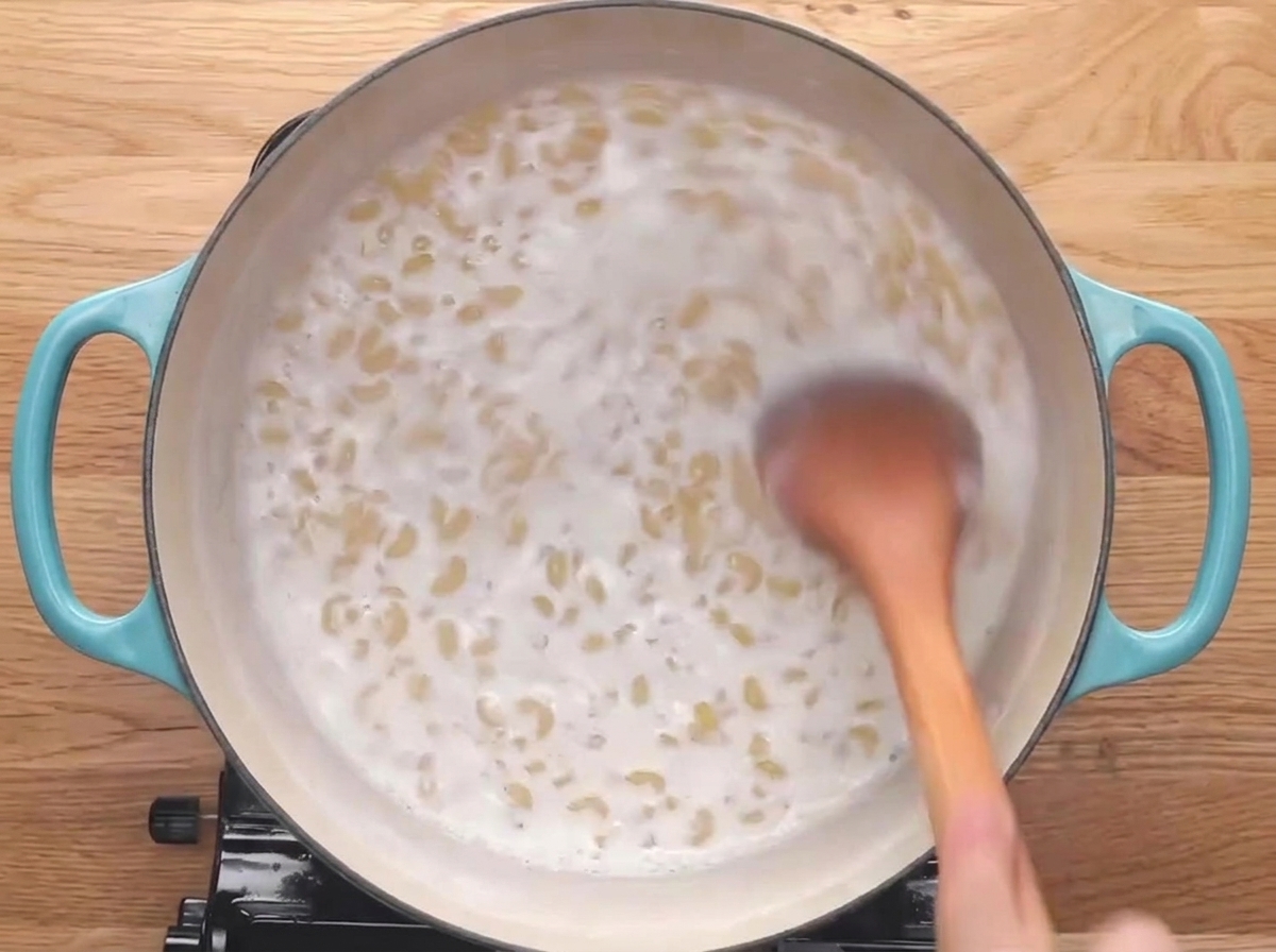Un cucchiaio di legno che mescola la pasta mentre sobbolle nel latte.