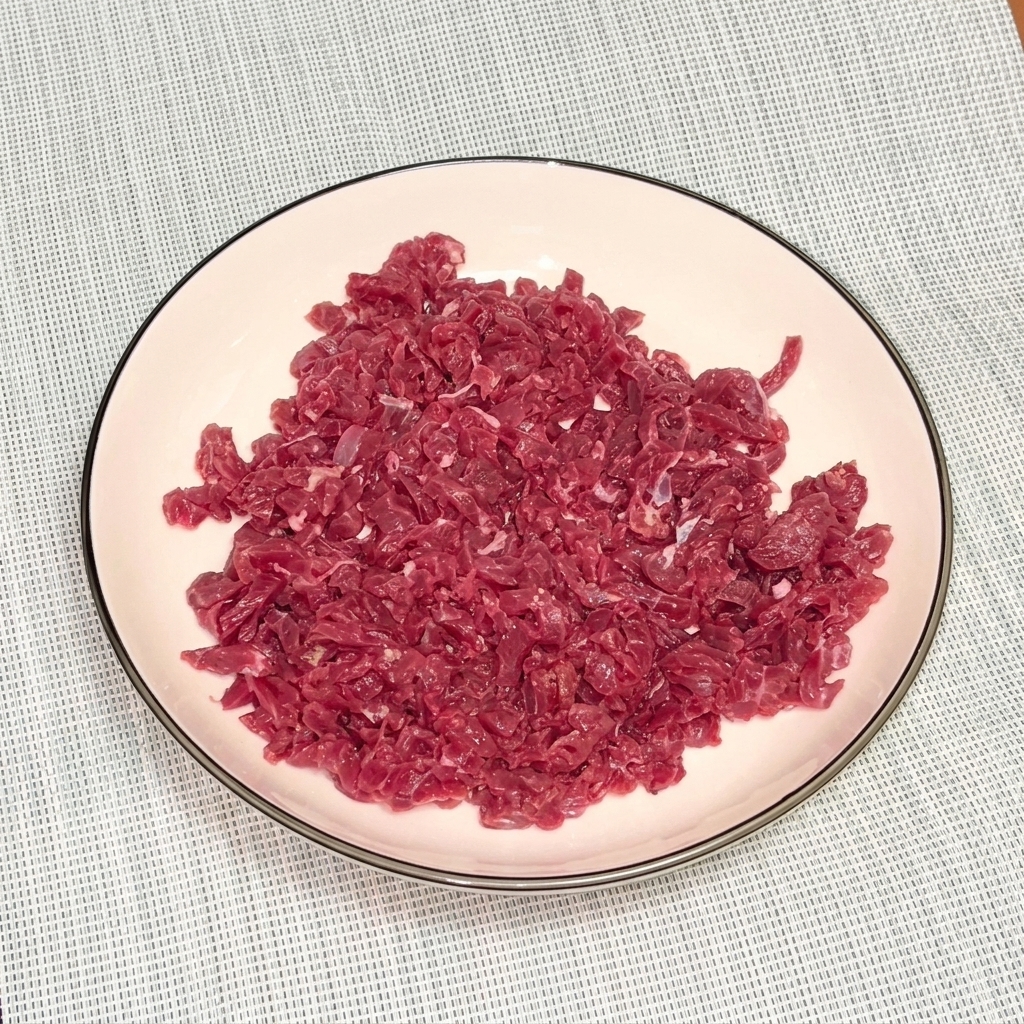 Carne macinata di manzo cruda in una ciotola bianca condita con pepe nero e olio per la marinatura.