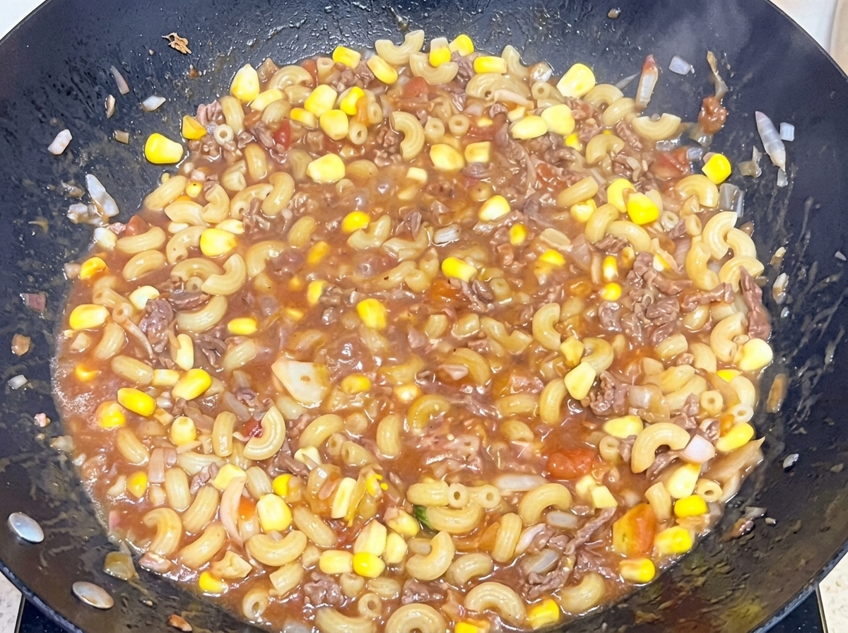 Maccheroni cotti mescolati a un saporito sugo di manzo e pomodoro in un grande wok.